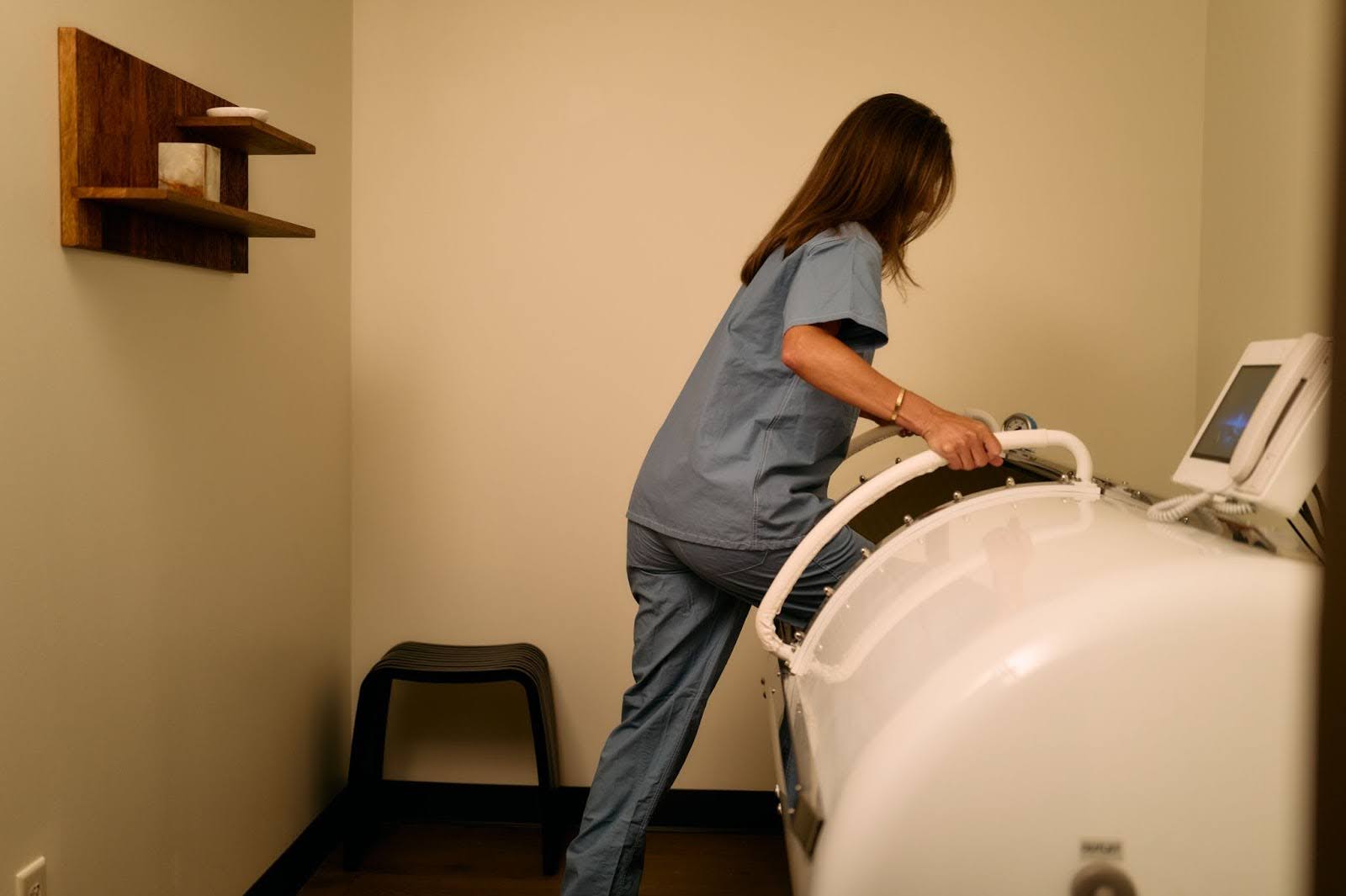 A hyperbaric oxygen therapy chamber sits in the middle of a treatment room while a patient gets in.