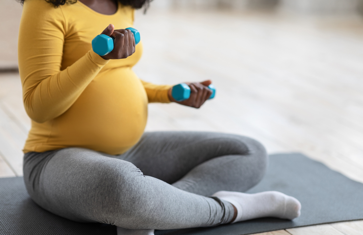 A woman at the end of her second trimester lifts low-impact weights while sitting on a yoga mat.