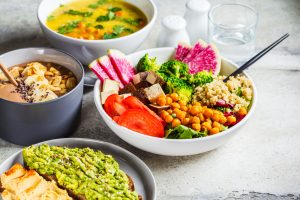 A table is covered in various colorful meals, including soup, a rice bowl, and avocado toast.