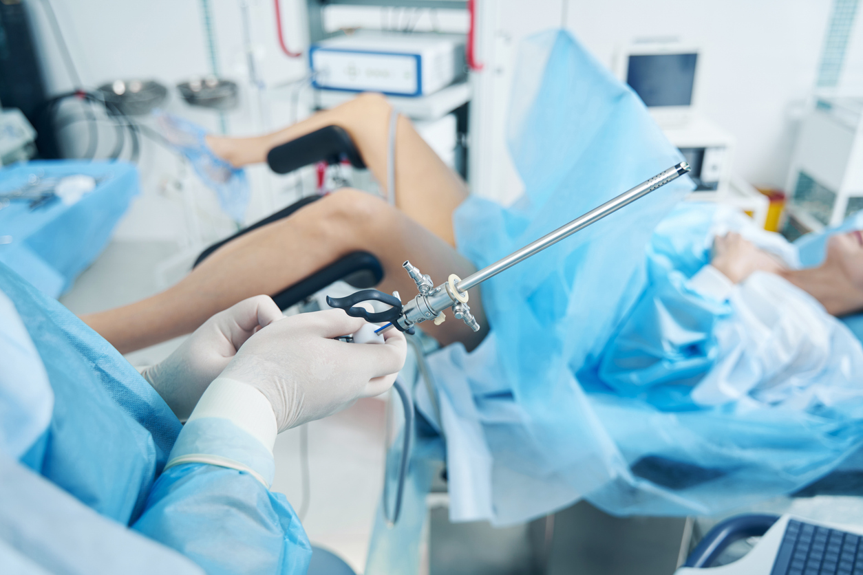 A fertility doctor holds a hysteroscope while a patient lies in a gynecology chair.