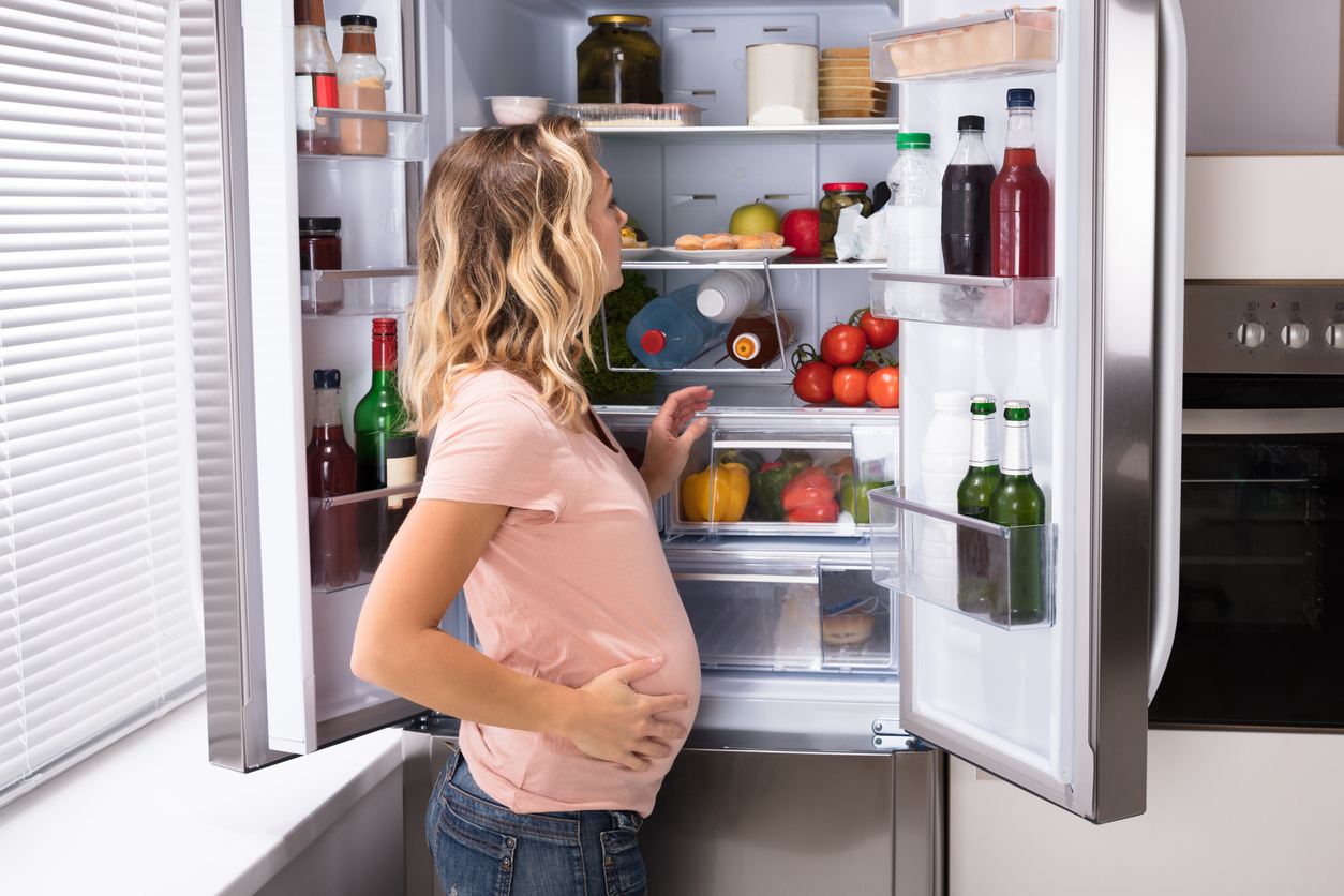 A young pregnant woman looks for something healthy to eat in the refrigerator.